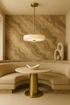 Modern interior design with a round table, beige sofa, and abstract sculpture against a marble-patterned wall. Satin Brass alabaster pendant LED. 