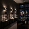 Dark interior of a high-end store with mannequins and shelves displaying luxury items with glass wall sconce.