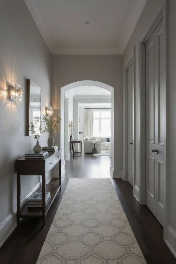 Long hallway with a patterned rug, side table, and mirror and glass wall sconces.