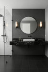 Modern bathroom with black marble vanity, round mirror, and matte black alabaster LED wall lights.
