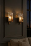 Wall-mounted glass and metal lights with textured glass panels on a dark wall.