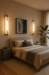 Modern bedroom with a bed, wall alabster matte black sconces, and a plant.