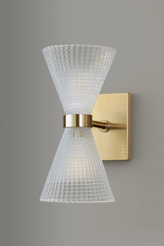 Wall-mounted light fixture with glass cone shade and satin brass base on a gray background
