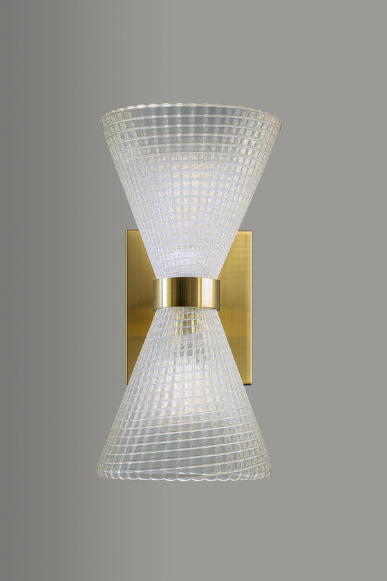 Wall-mounted light fixture with textured glass shade and satin brass base on a gray background