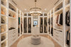 Modern walk-in closet with white shelves, drawers, and clothing racks. Chandelier satin brass with clear glass. 