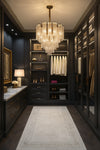 Luxurious walk-in closet with dark wood shelves, clothing, and a satin brass with water glass chandelier.