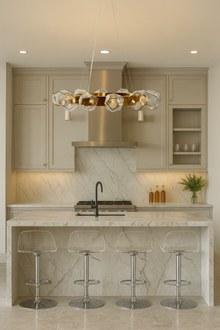  Modern kitchen with marble countertops, bar stools, and a decorative satin brass and glass chandelier.