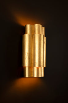  An elegant three-tiered wall sconce with a distressed gold finish, emitting a warm glow.