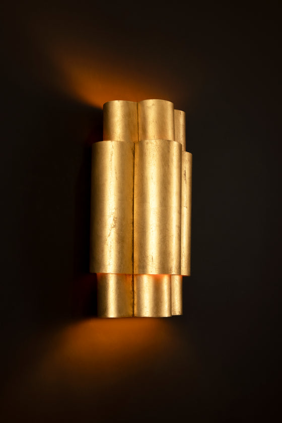 An elegant three-tiered wall sconce with a distressed gold finish, emitting a warm glow.