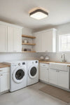 Modern laundry room with white washer and dryer, wooden countertops, and cabinets. Matte Black square LED ceiling light.