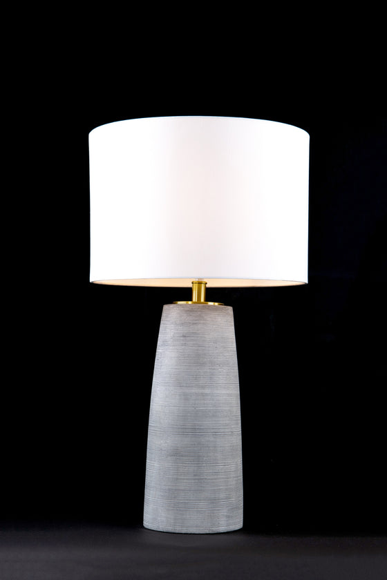 A Harper geometric grey ceramic table lamp with satin brass and a white fabric shade on a black background