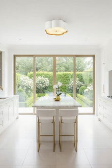  Modern kitchen with white island and stools, large window view of garden. Flushmount white flower design ceiling light.