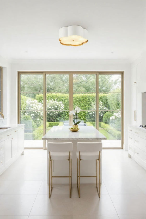 Modern kitchen with white island and stools, large window view of garden. Flushmount white flower design ceiling light.
