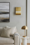 Modern living room with a beige sofa, gold lamp, and abstract painting. LED satin brass wall sconces. 