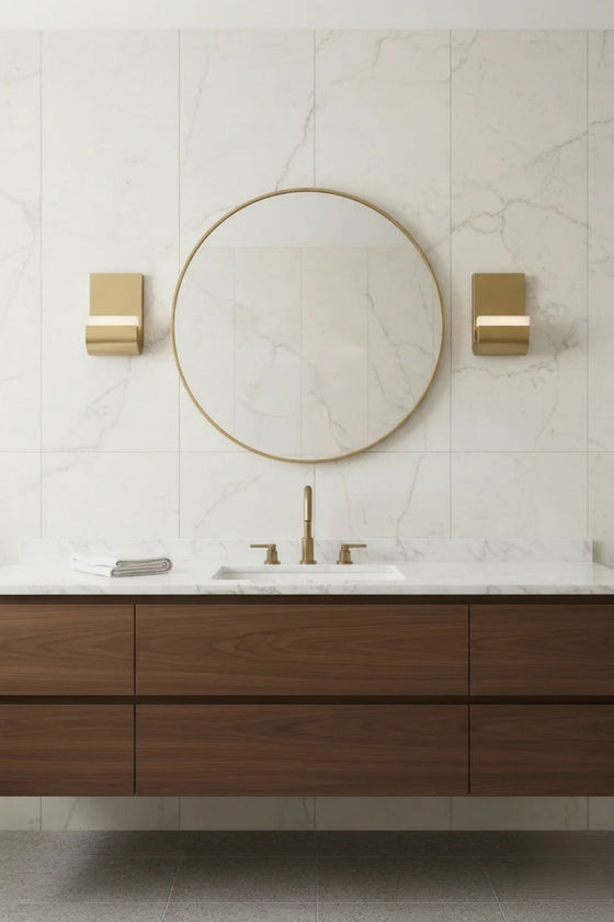 Bathroom vanity with round mirror, wooden cabinets, and LED satin brass wall sconces.