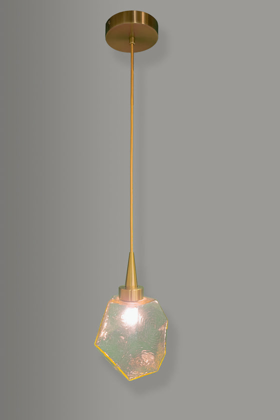 Modern pendant light with amber geometric glass shade and brass fixture on a gray background