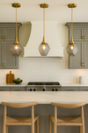 Modern kitchen with satin brass and smoke glass pendant lights, stove, and island chairs.