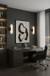 Modern home office with dark wood desk, chair, and abstract art on gray wall. Alabaster bronze wall LED sconce.