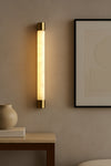Wall-mounted LED alabaster satin brass light fixture on a neutral wall with a framed abstract art piece.