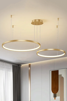  Two contemporary round pendant ceiling lights with a satin brass finish, integrated LED lighting, and adjustable hanging cables, installed in a room with a white ceiling.