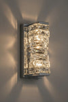 Modern polished chrome LED wall sconce with crystal-like design on a gray wall