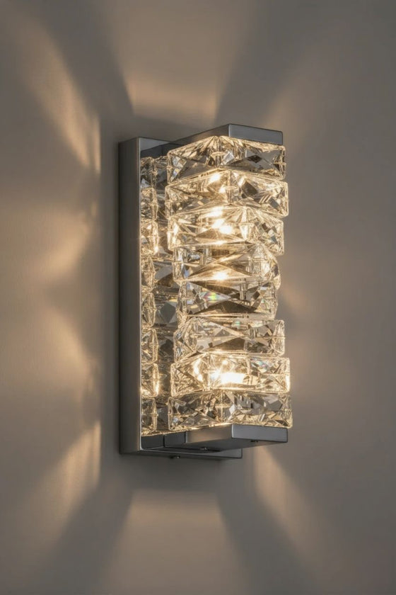 Modern polished chrome LED wall sconce with crystal-like design on a gray wall