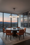 Dining room with round table and chairs, large windows showing a desert landscape, and framed pictures on the wall. Satin Brass LED chandelier.