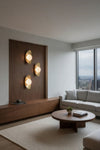 Modern living room with wooden wall panel, round coffee table, and city view. Satin brass LED sconce.