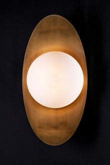  A LED wall sconce featuring a satin brass leaf-shaped backplate with a spherical milk glass orb.