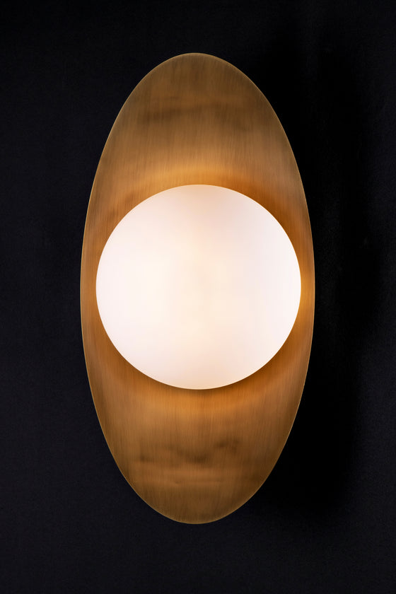 A LED wall sconce featuring a satin brass leaf-shaped backplate with a spherical milk glass orb.