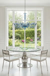 Dining room with a round table and chairs under a blue glass chandelier, large window showing a garden view.