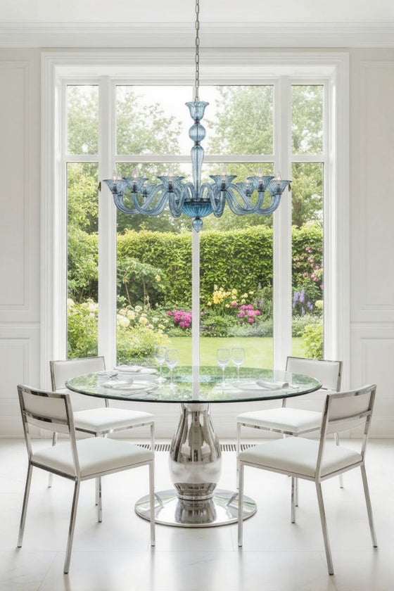 Dining room with a round table and chairs under a blue glass chandelier, large window showing a garden view.