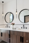 Matte Black Pendants Modern bathroom with wooden vanity, round mirrors, and pendant lights.