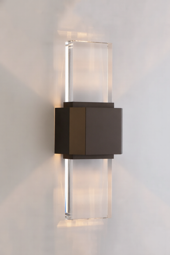 Modern wall-mounted bronze and glass light fixture on a plain wall.