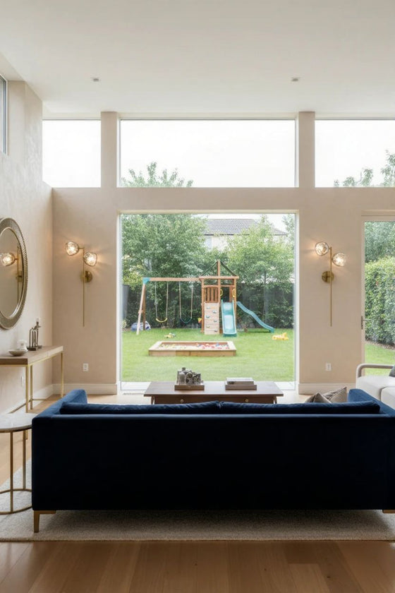 Modern wall sconce living room with a blue sofa, large windows, and a view of a backyard with playground equipment.