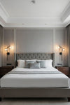 Modern matte black sconces in bedroom with a gray upholstered bed, white bedding, and wall sconces.