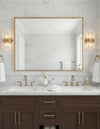 Bathroom vanity with marble countertop, satin brass light fixtures, and large mirror.