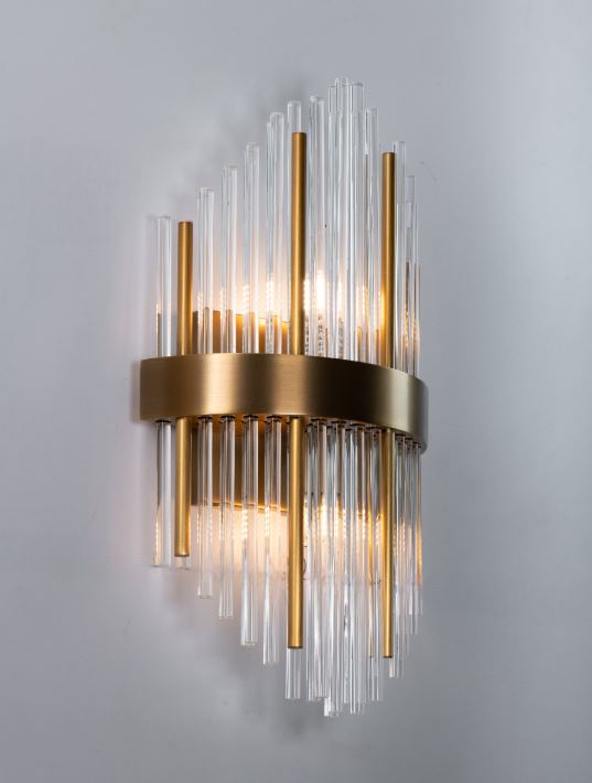 A contemporary wall sconce with staggered glass tubes and a satin brass band, set against an indoor wall.