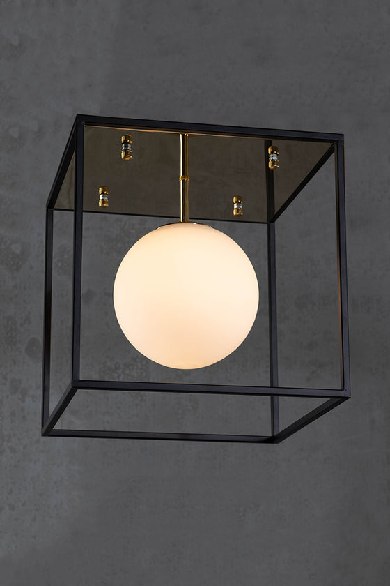 A contemporary style ceiling-mounted light fixture with a polished brass canopy and a matte black frame, featuring a white globe.