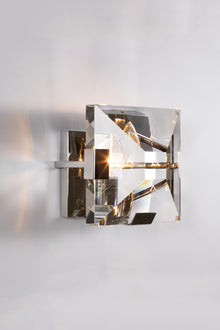  A contemporary polished stainless steel wall sconce with a clear glass lens and metallic frame, illuminated to showcase the lighting effect.