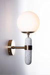 A modern wall sconce featuring a faux concrete body with a satin brass finish on the backplate and opal glass globe.
