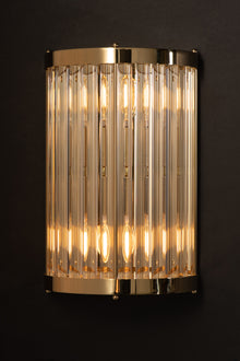  A wall-mounted sconce with a satin brass finish and clear glass rods, glowing warm white light.