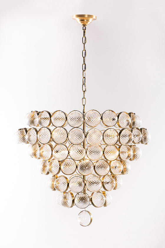 A satin brass chandelier with ribbed glass globes and brass metal rings, against a white background.
