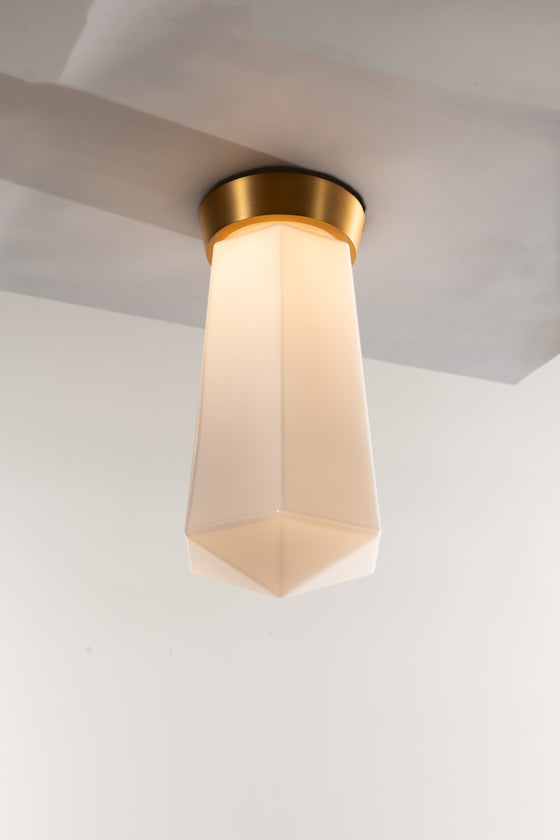 A LED ceiling light fixture with a geometric shape and a matte opal glass shade, featuring a satin brass finish.