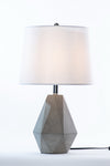 A contemporary geometric table lamp with a natural gray concrete base and a white fabric shade, with a black cord.