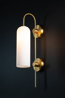  A wall-mounted light fixture with a brass finish and frosted opal glass shade, displaying a warm, ambient glow.