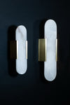 An oval-shaped wall sconce with a white alabaster shade and a satin brass finish, displaying a warm light LED glow.