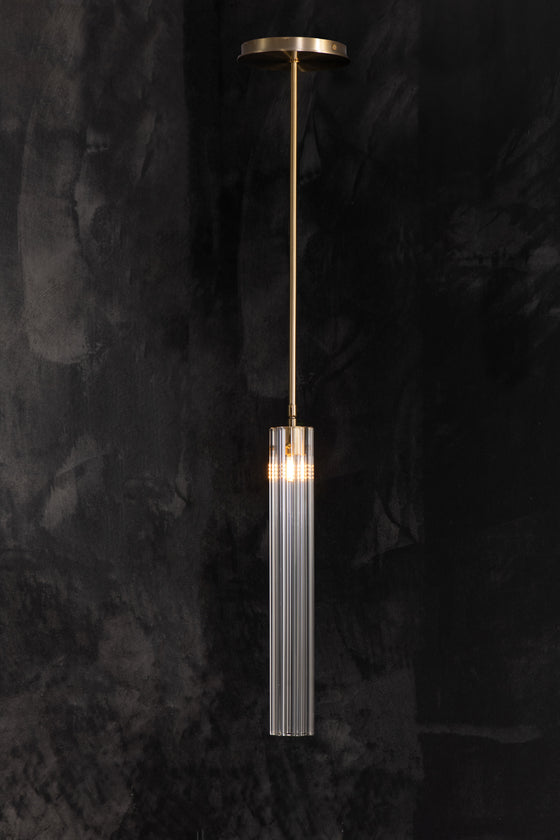 A fluted glass pendant light with a metallic finish hanging against a dark background, showcasing a sleek and modern design.