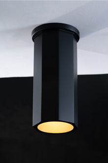  A black Octavia downlight installed on a ceiling, with light shining down from its cylindrical metal shell.