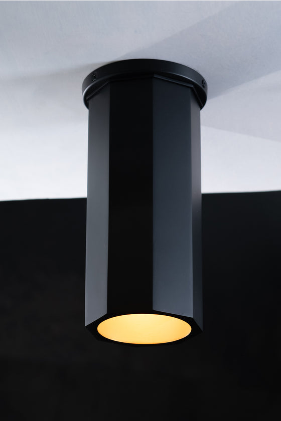 A black Octavia downlight installed on a ceiling, with light shining down from its cylindrical metal shell.